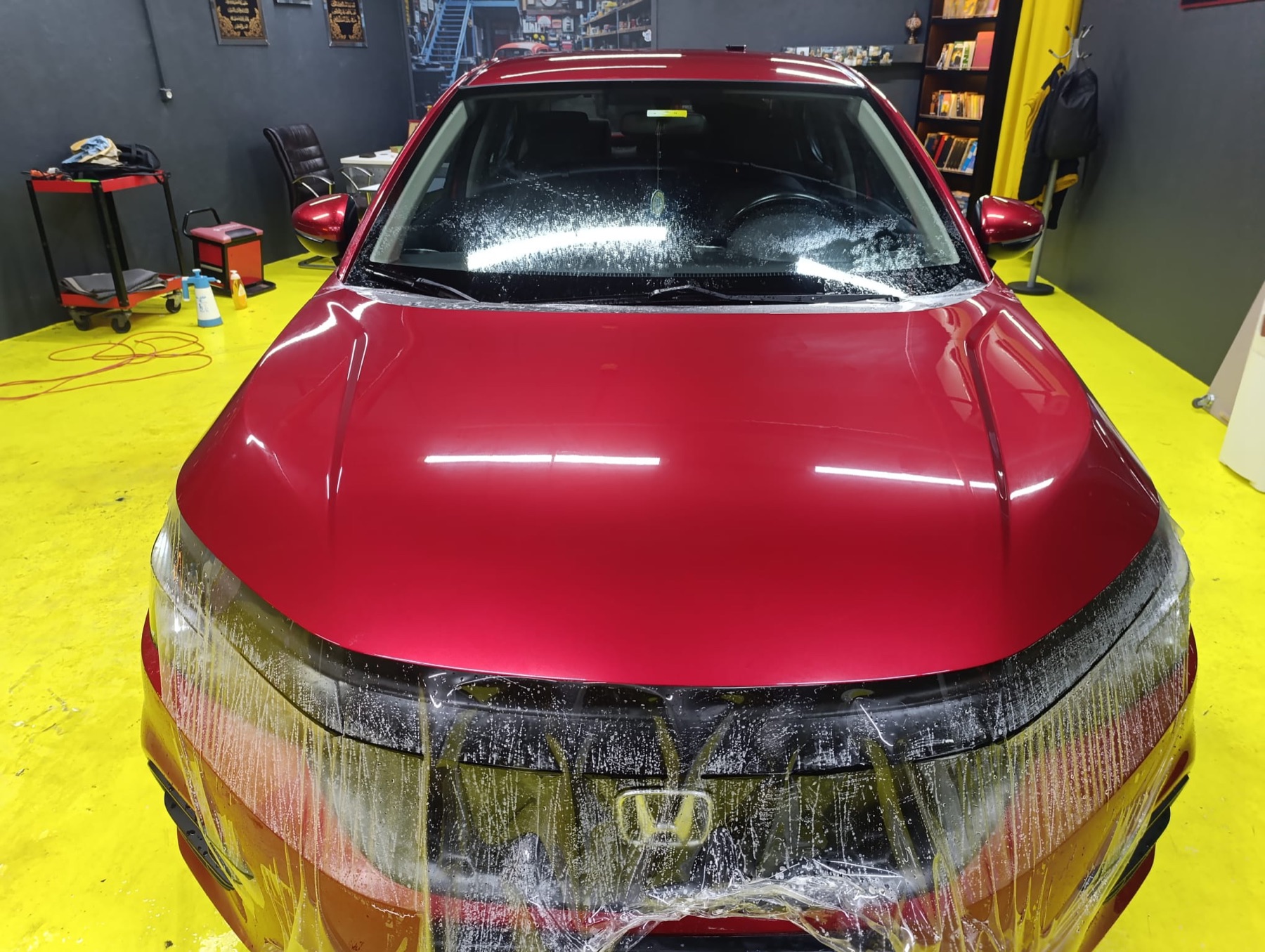 Kırmızı Honda Civic'in kaputuna koruma filmi serilirken